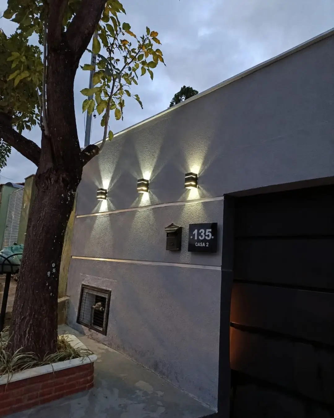 Fachada residencial com muro cinza iluminado à noite, Belo Horizonte